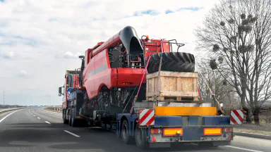 Heavy industrial truck with semi trailer platform transport disassembled combine harvester machine on common public highway road on sunset sunrise day. Agricultural equipment transportation service